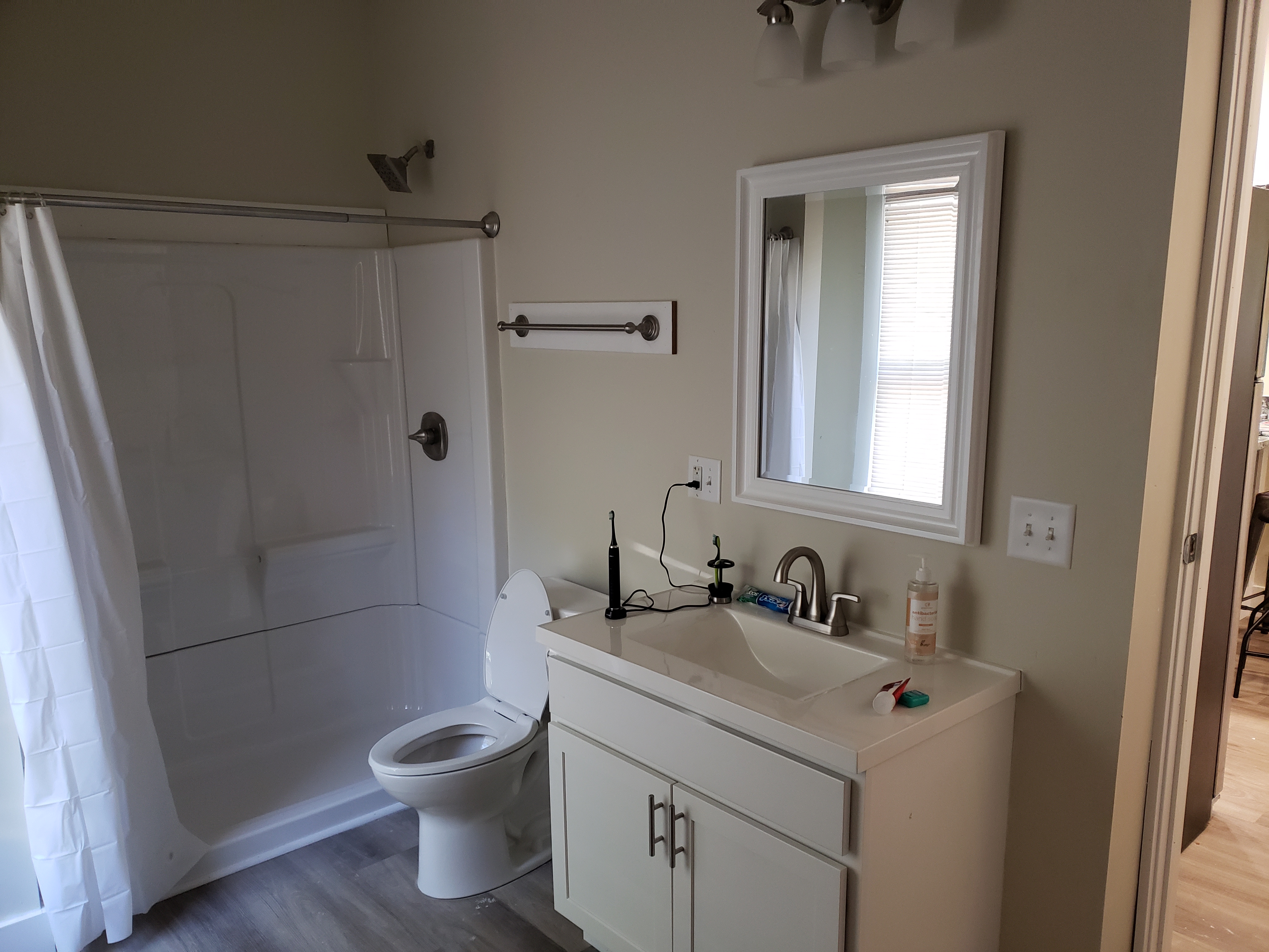 White shower/tub combo unit in a bathroom undergoing renovation; brown framing and tan wall