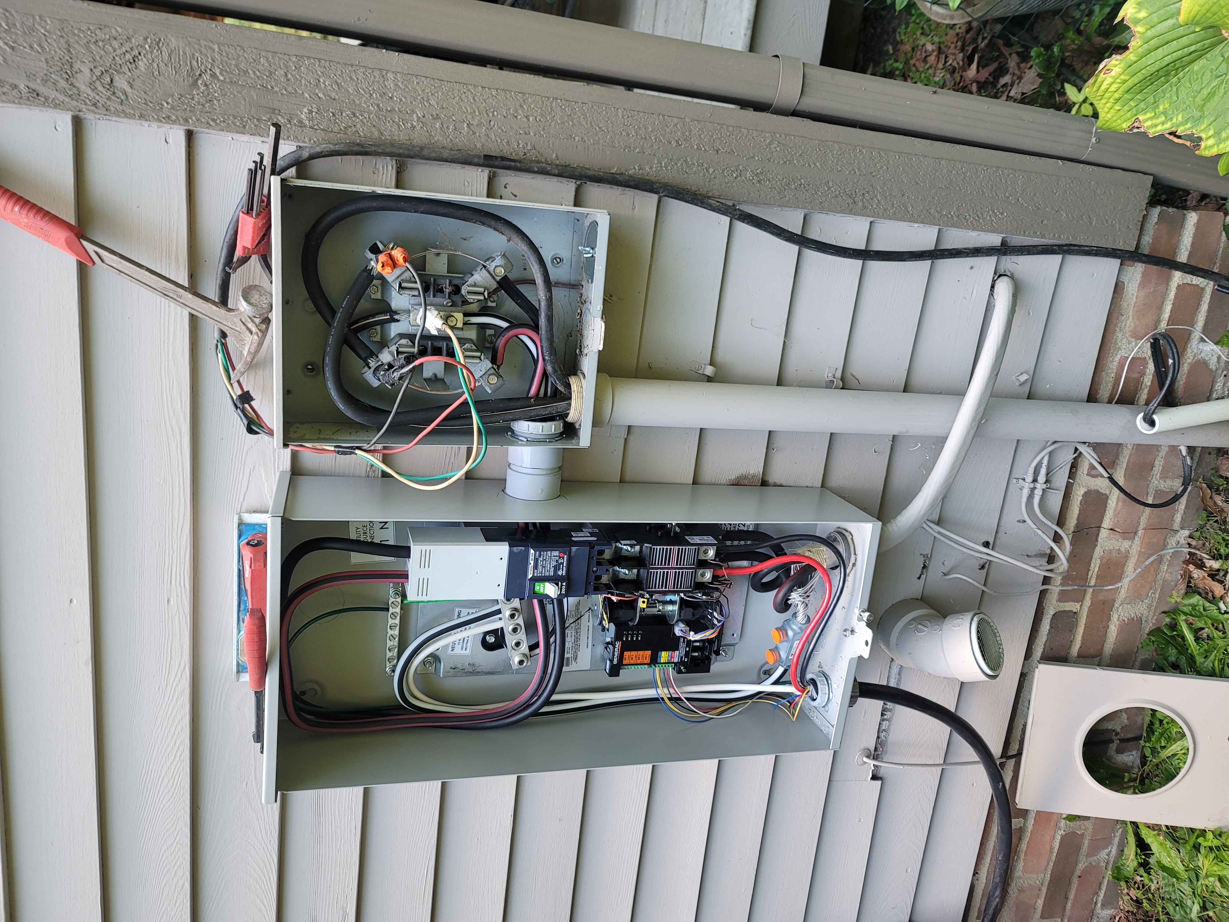 Electrical panel mounted on plywood in a basement, wiring visible; a power drill and other tools nearby