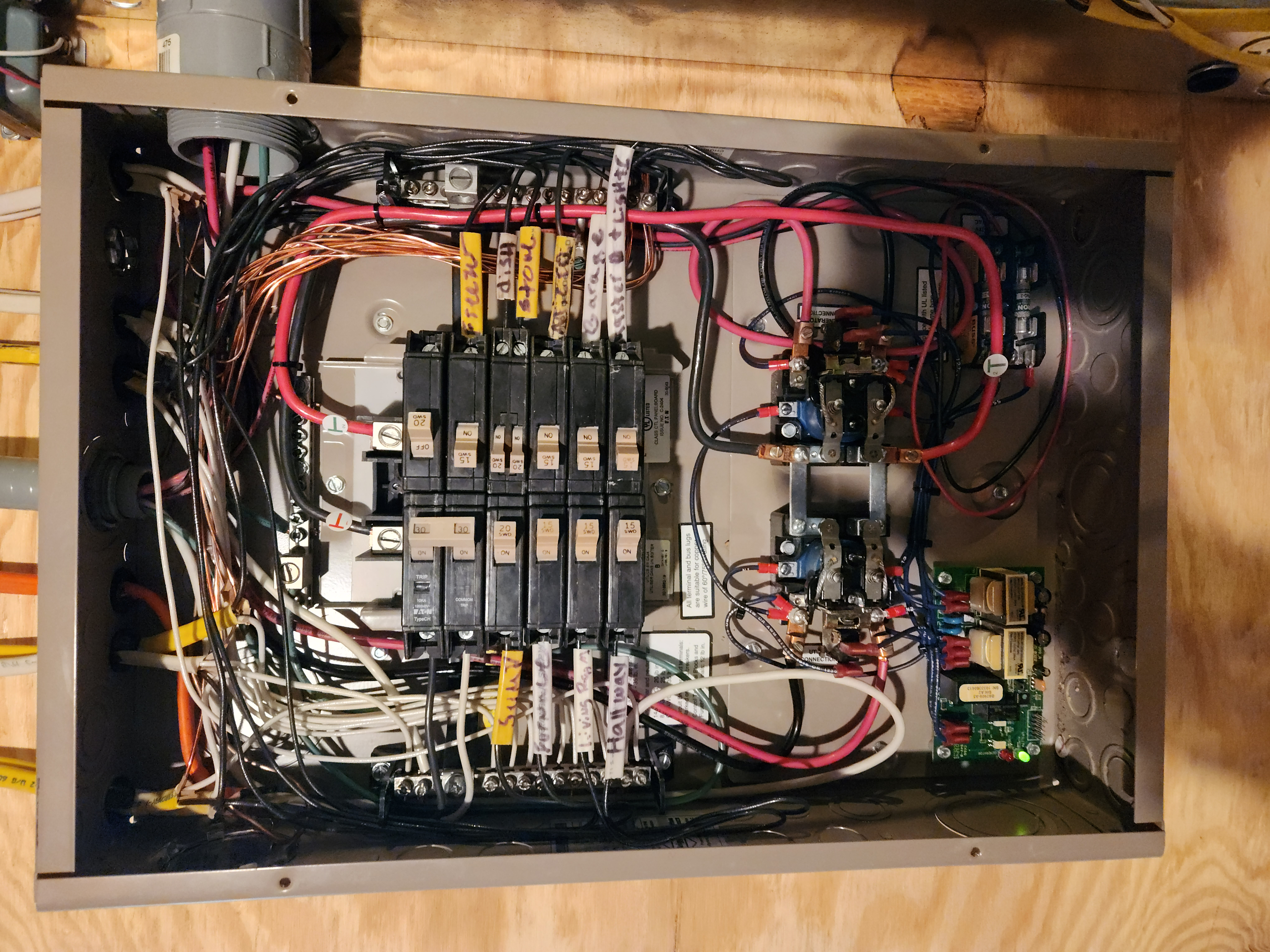 Open gray electrical panel with circuit breakers, installed in a wooden wall