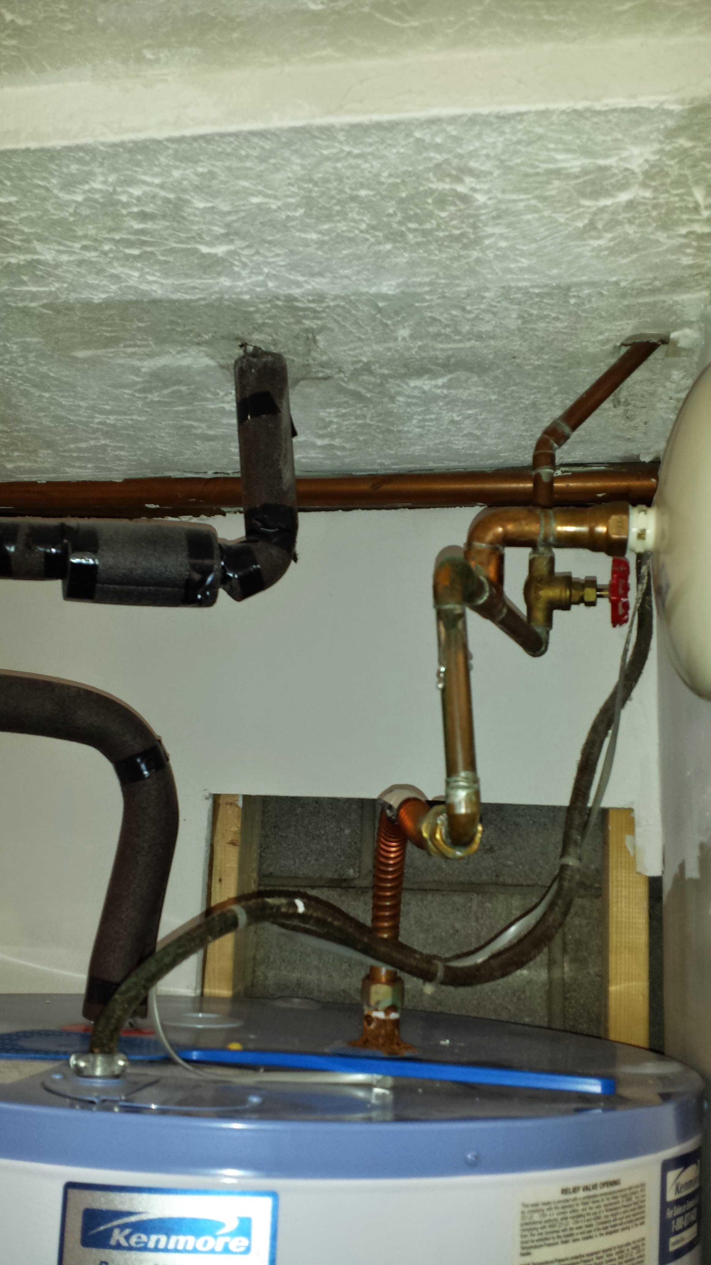 Tankless water heater installed on a concrete wall, with blue and red pipes and a white expansion tank