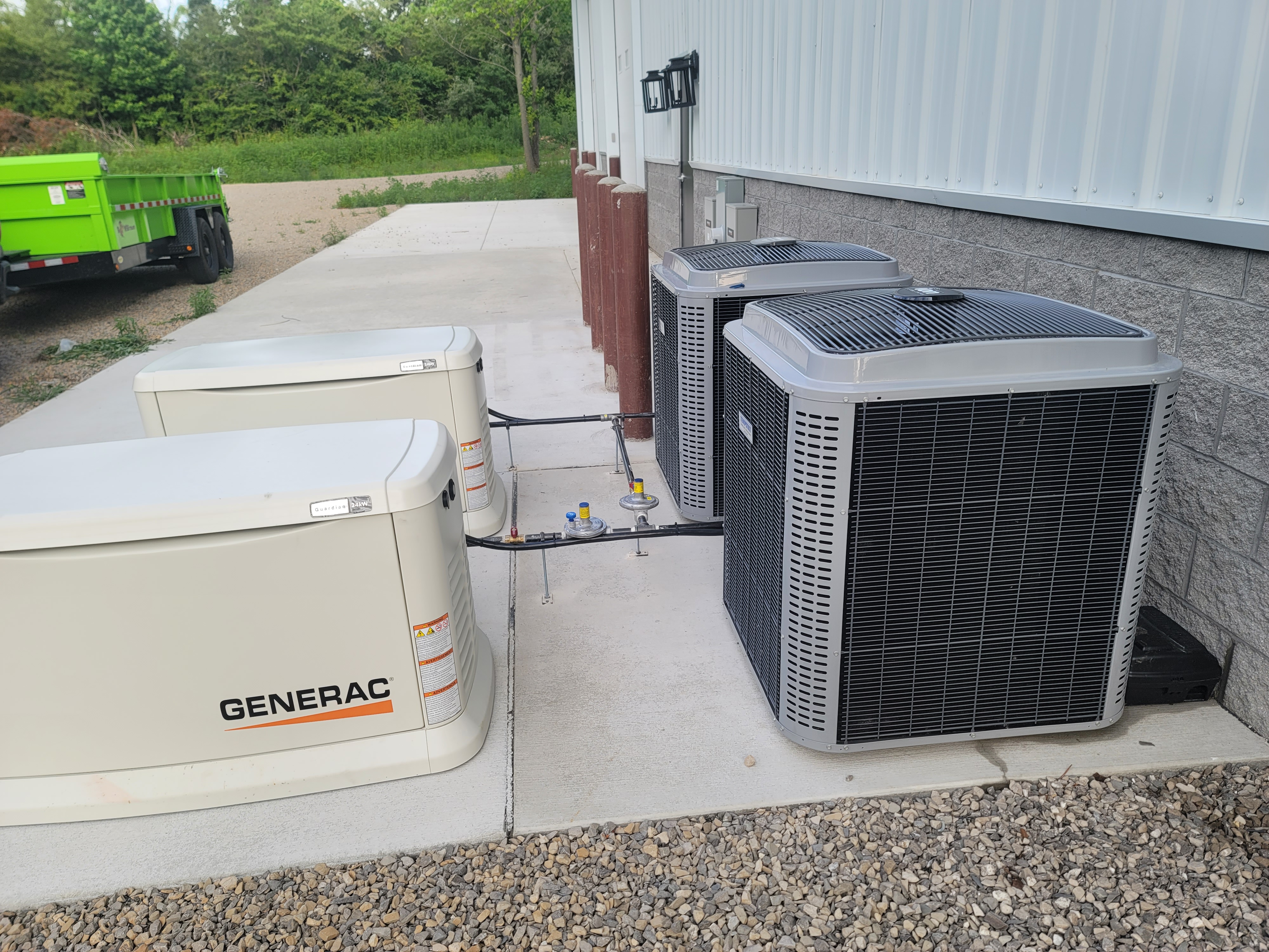 Two Generac generators and two gray HVAC units sit next to a white building on a concrete pad