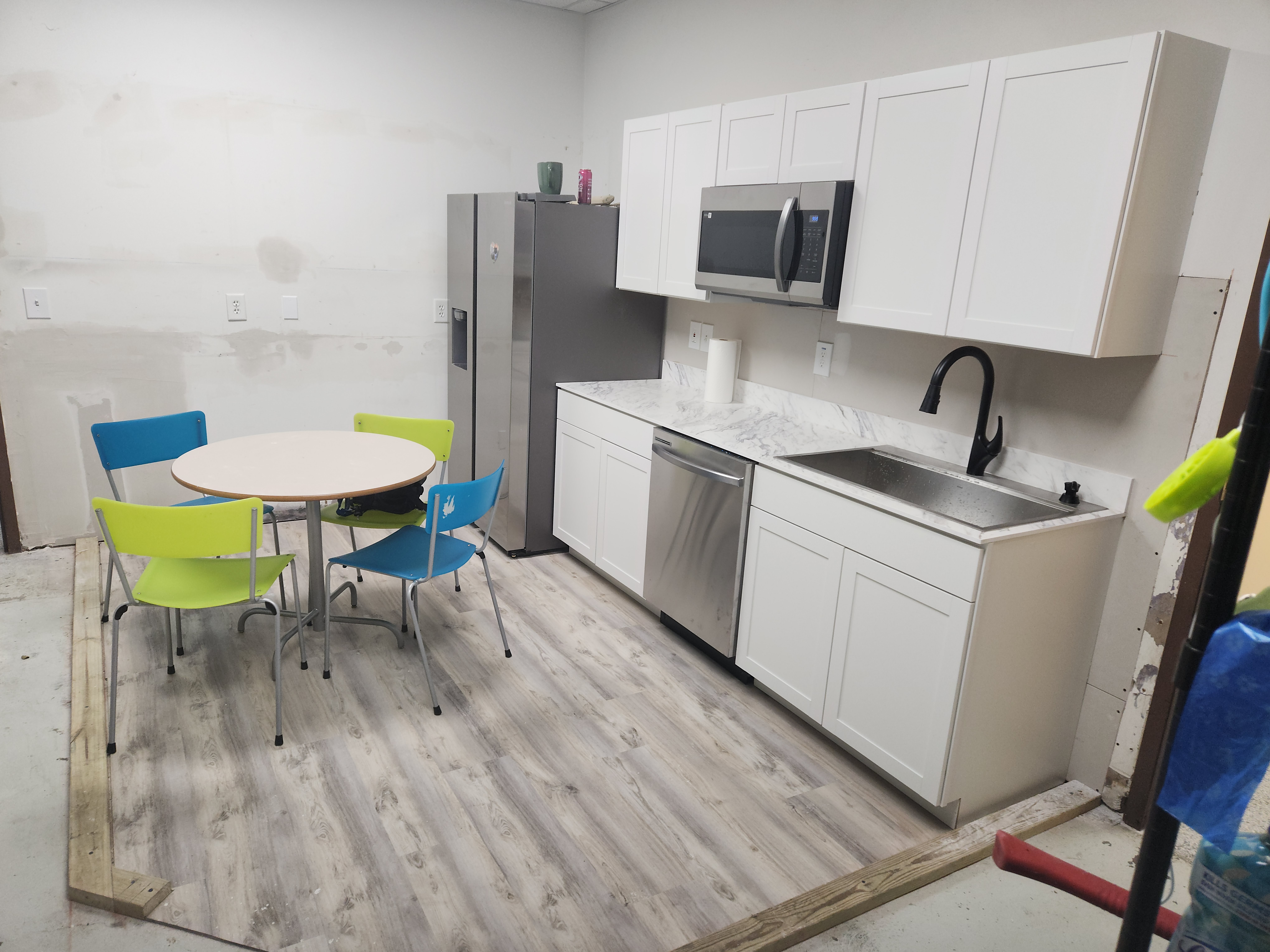 Small office kitchen with white cabinets, stainless steel appliances, table, and colorful chairs