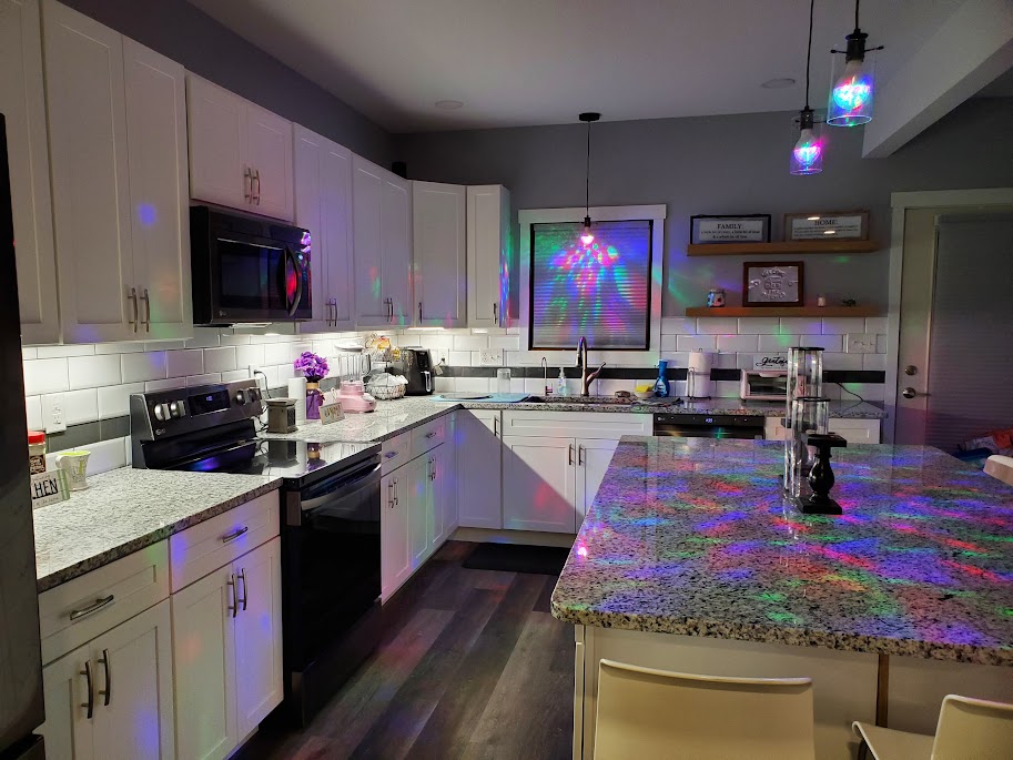 Kitchen with white cabinets, granite countertops, stainless steel appliances, and colorful lights